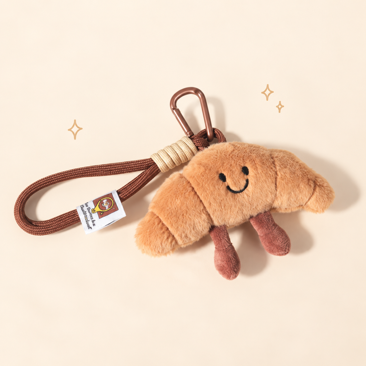 Croissant Buddy Plush Charm on a softly lit cream and pastel background.