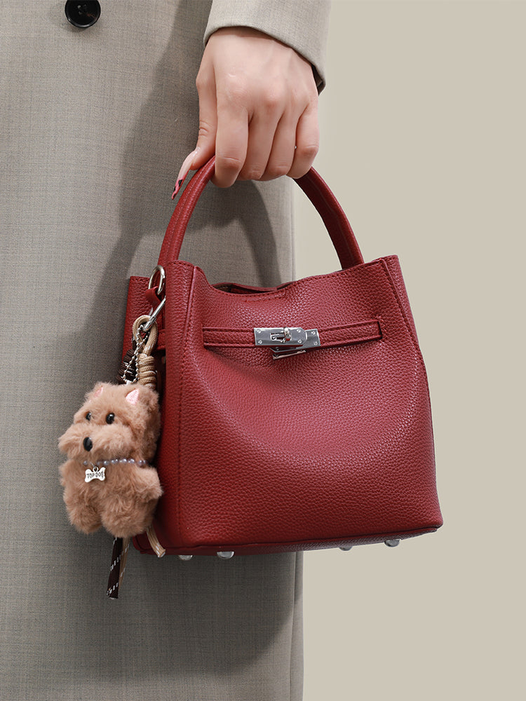Wine red mini bucket bag carried by its top handle beside a grey coat