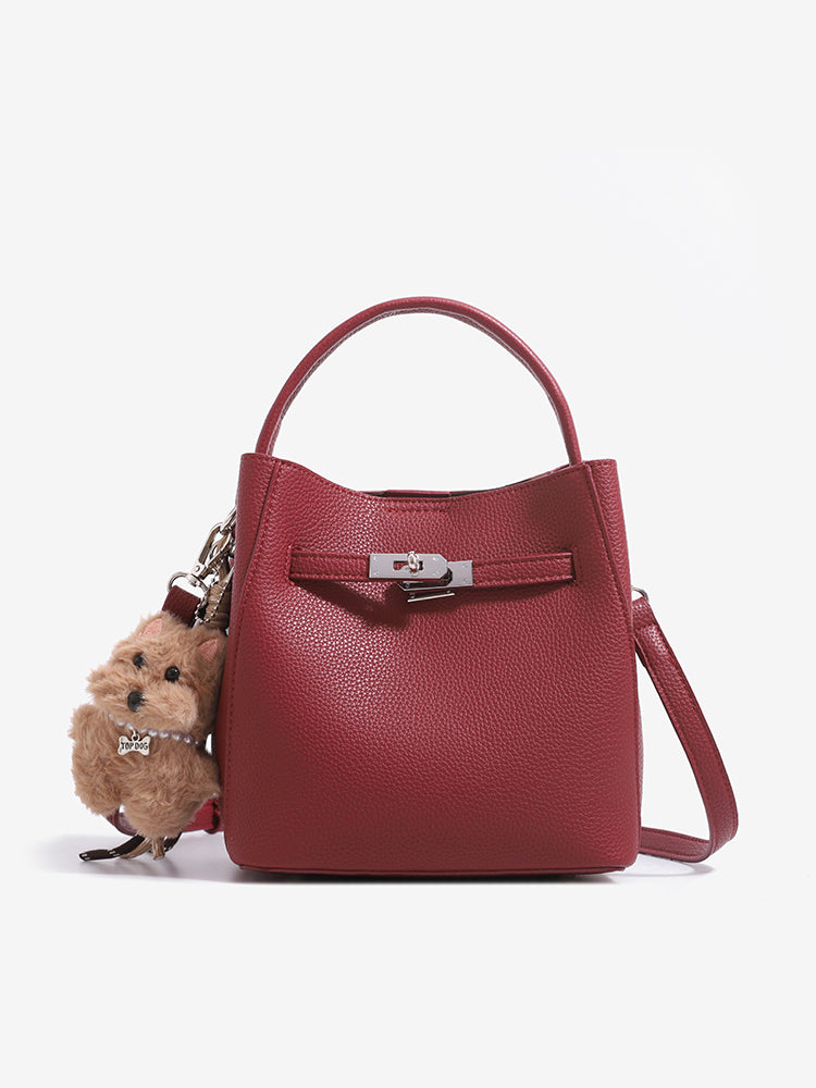 Wine red mini bucket bag with top handle, shoulder strap and plush dog charm on a white background