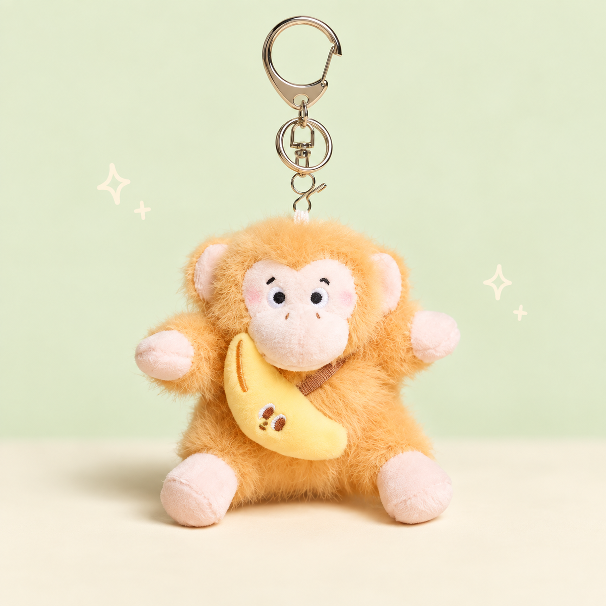 Banana Monkey Plush Charm on a softly lit cream and pastel background.
