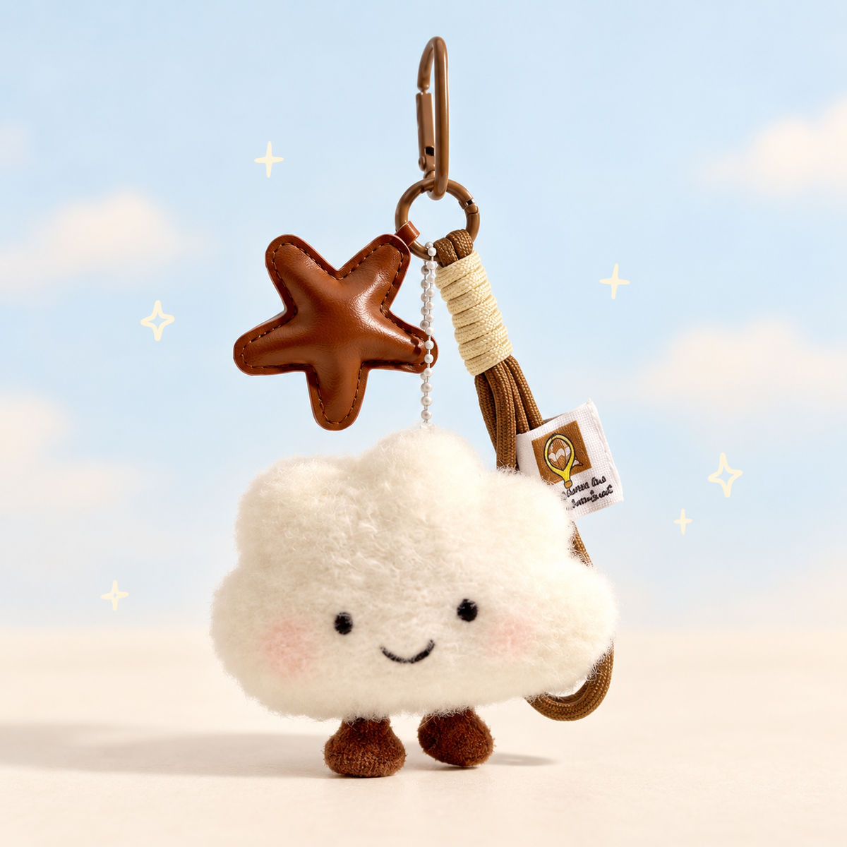 Smiling white cloud plush keychain with a brown star charm and rope loop on a pale blue and cream background.