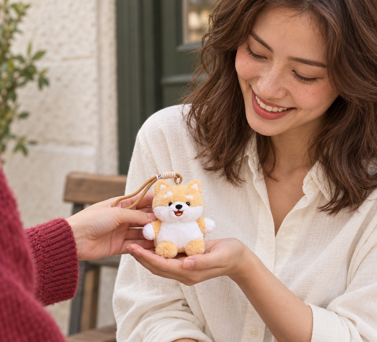 A smiling woman receiving a small puppy plush keychain from a friend in a raspberry cardigan.