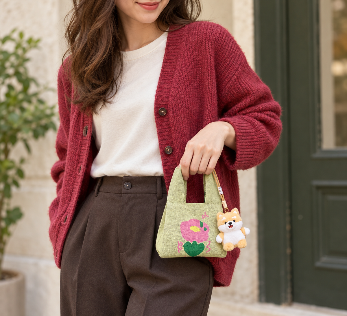 A woman in a raspberry cardigan carrying a small green knitted flower bag with a puppy charm.